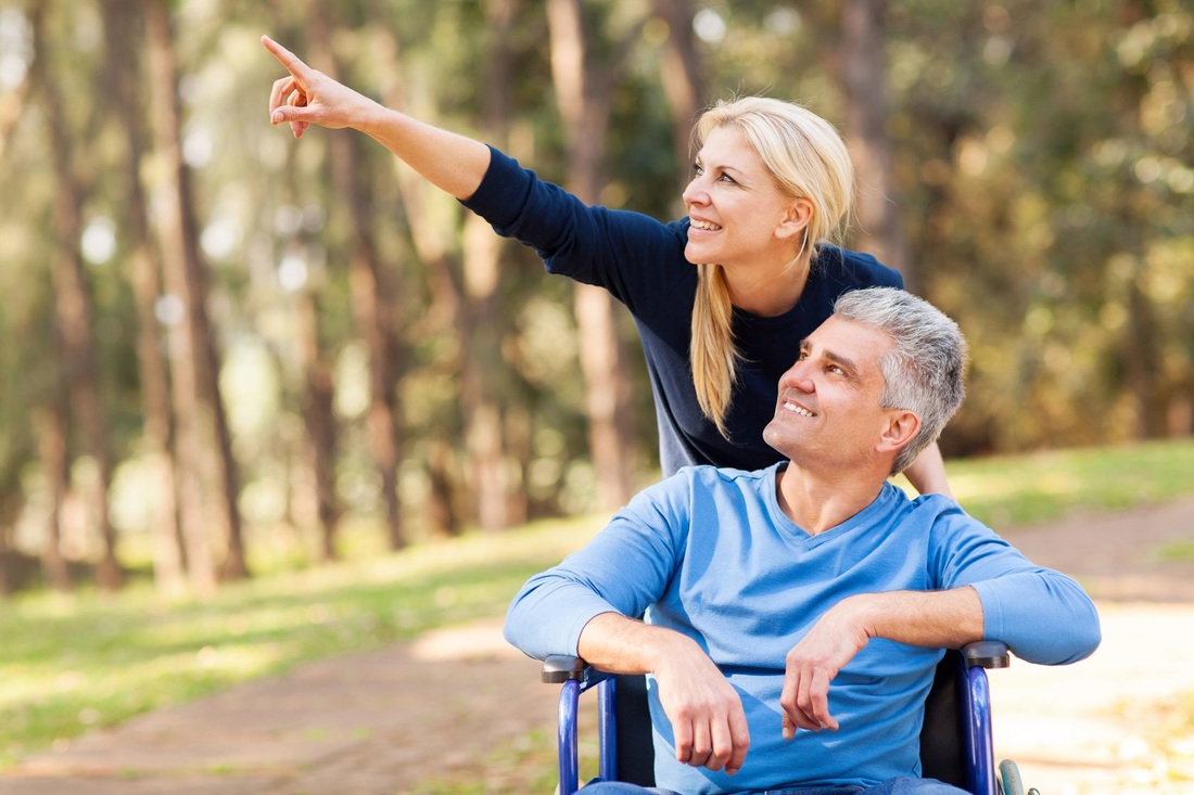 Picture of man in wheelchair with caregiver pointing upward while enjoying a stroll outdoors