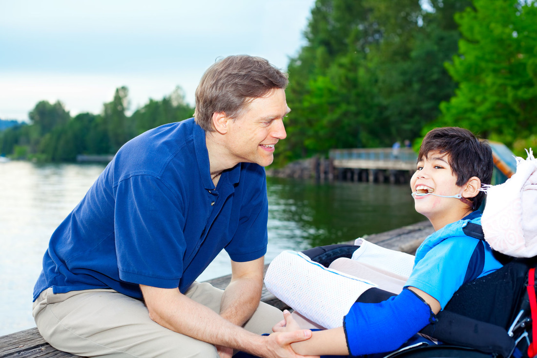 Picture of a young boy receiving assistance by a caregiver near a body of water